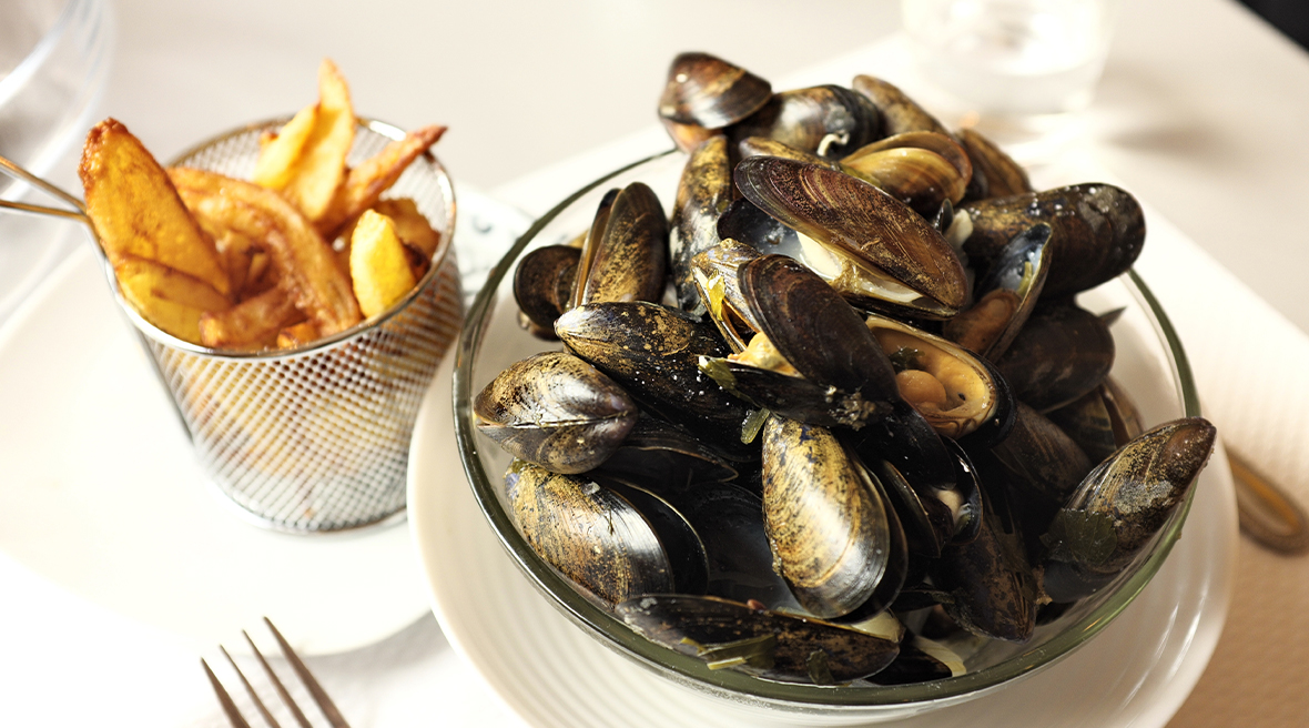Bowl of mussels next to a metal mesh container of chips at a restaurant table